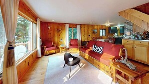 Un intérieur de chalet chaleureux, avec un revêtement en bois, un canapé, des fauteuils, une table à manger et un coin cuisine.