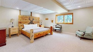 Un dormitorio con cama de madera, mesitas de noche, una silla, una ventana e iluminación empotrada en el techo.