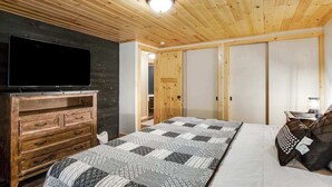 Een slaapkamer met een houten plafond, een bed met beddengoed met een patroon, een televisie op een houten dressoir en een garderobe.