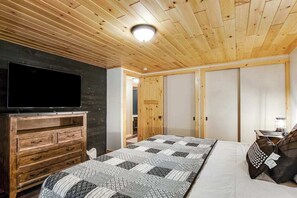 A bedroom with a wooden ceiling, a bed with patterned bedding, a TV on a wooden dresser, and a wardrobe. - Renovated lake-view retreat with full rec lake access, boat slips, & firepits (St. Germain)