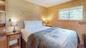 A wooden-paneled bedroom with a bed, two bedside lamps, a window, and a nightstand. - Rustic Cozy lakefront Cabin with dock, fire pit, gas grill, W/D & quiet location (St. Germain)