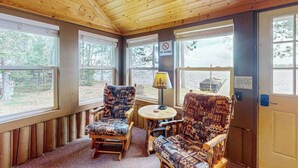 A cozy cabin interior with wooden walls and large windows, two patterned chairs, a small table with a lamp, and a 'NO DIVING' sign. - Rustic Cozy lakefront Cabin with dock, fire pit, gas grill, W/D & quiet location (St. Germain)