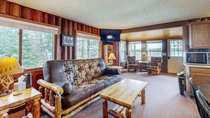 A cozy cabin interior with a leather sofa, wooden coffee table, and a television mounted on the wall. - Rustic Cozy lakefront Cabin with dock, fire pit, gas grill, W/D & quiet location (St. Germain)