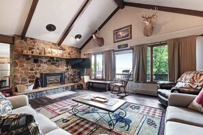 Ein gemütliches Wohnzimmer mit Kamin aus Stein, einer Couch, einem Couchtisch und einem Hirschgeweih an der Wand.