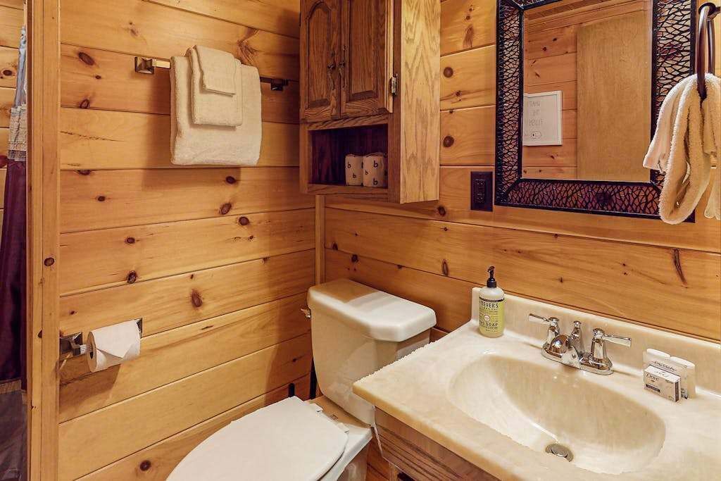 Un baño estilo cabaña de madera con inodoro, lavamanos y armarios.