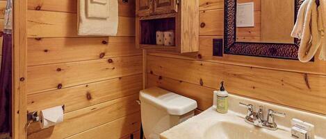 Un baño estilo cabaña de madera con inodoro, lavamanos y armarios.