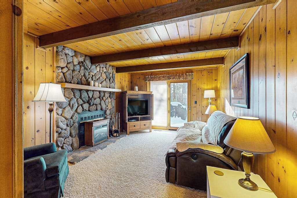 L’intérieur chaleureux d’un chalet avec une cheminée en pierre, un téléviseur, un canapé et une lampe.