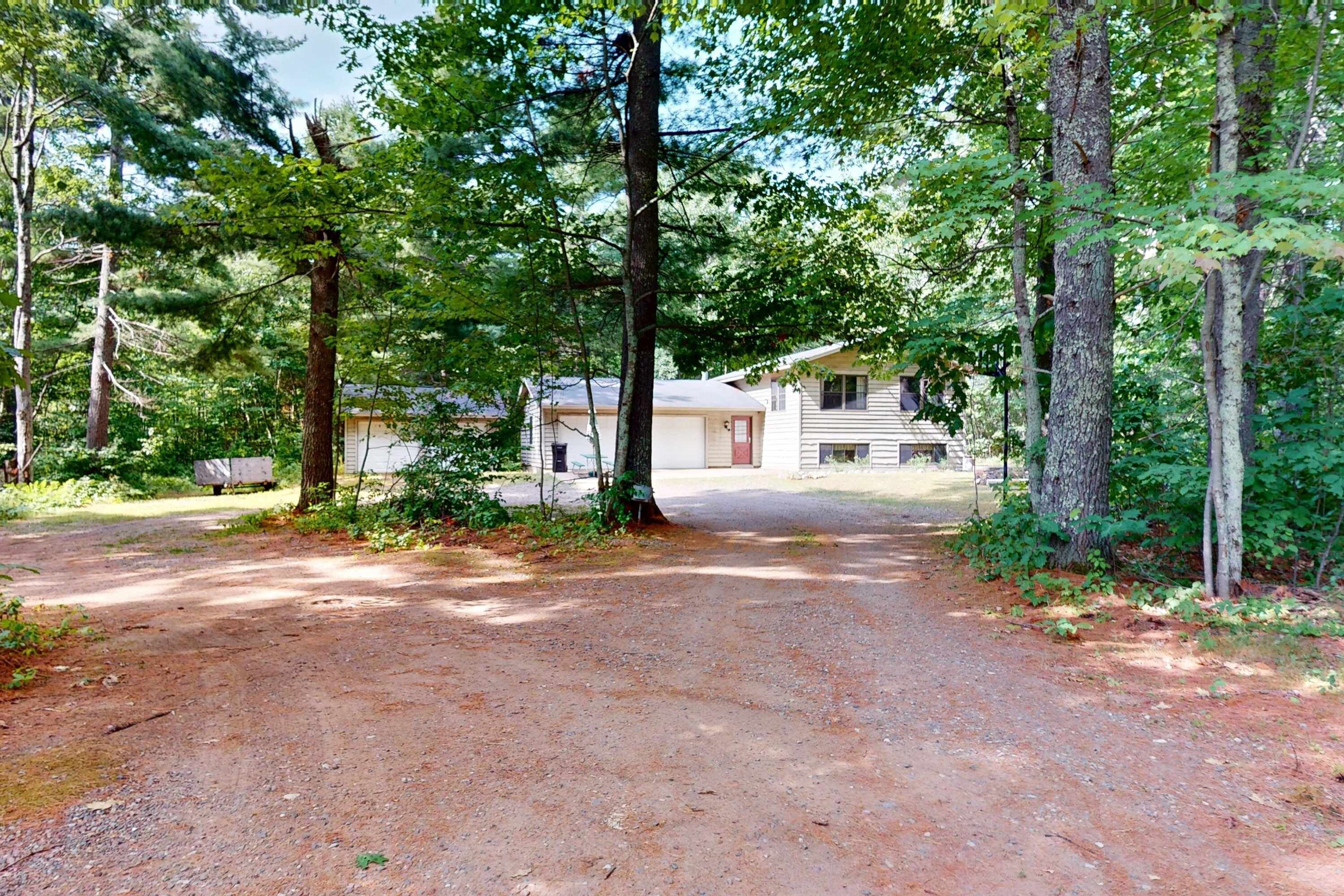 A rural property with a gravel driveway leading to a single-story house surrounded by dense trees.