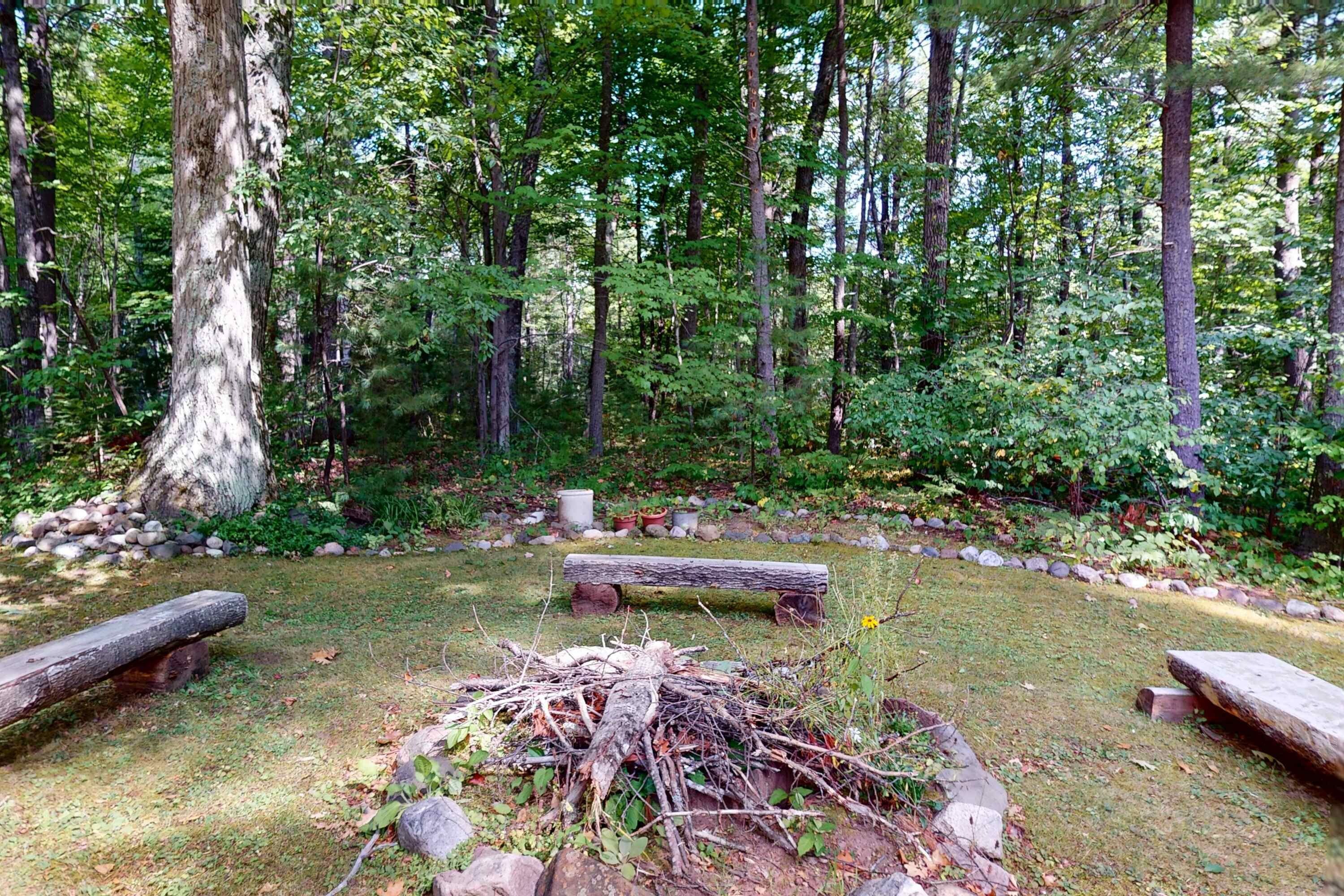 A forested area with a fire pit, benches, and a stone path.