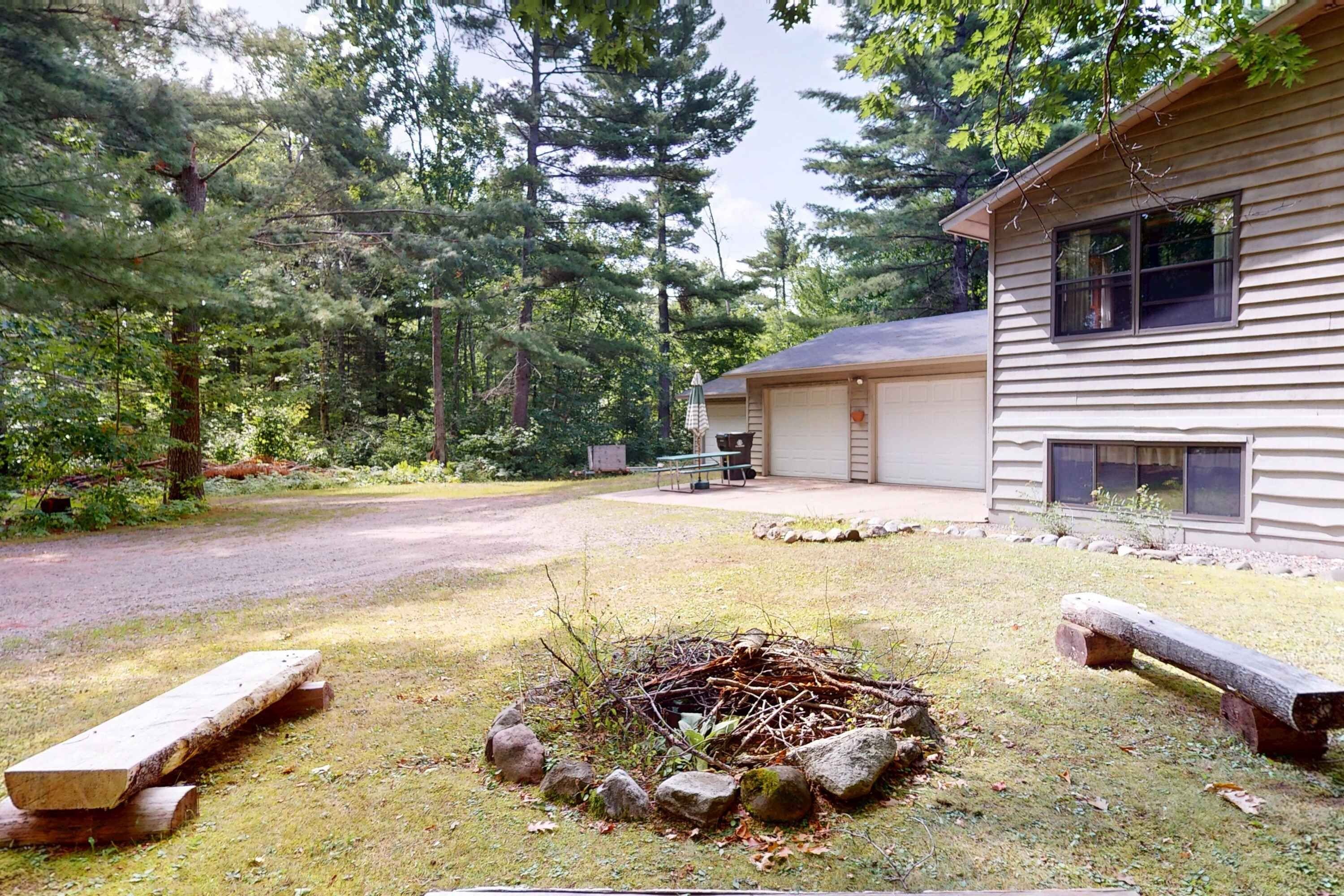 A house with a garage, a fire pit, and a picnic table in a wooded area.