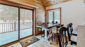 A wooden interior with a dining table and chairs, large windows, and a view of a snowy outdoor area. - Rustic resort cabin with lake views, deck & access to docks, canoe, paddle boats (Mercer)
