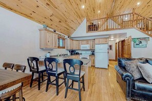 Eine geräumige Küche mit Holzausstattung, eine Essecke mit Stühlen, ein schwarzes Ledersofa und eine Treppe zu einer oberen Ebene.