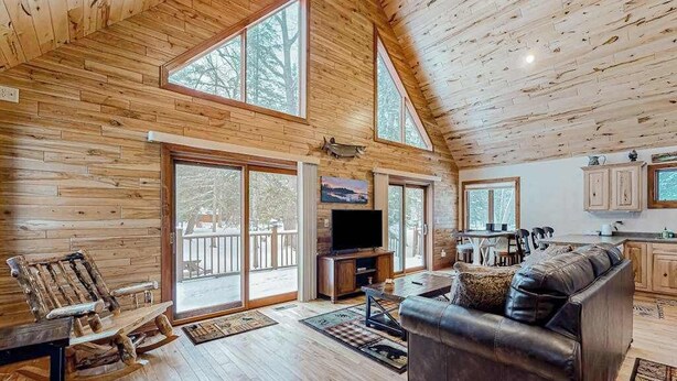 A spacious living area with a wooden ceiling, large windows, a fireplace, a sofa, and a television. - Rustic resort cabin with lake views, deck & access to docks, canoe, paddle boats (Mercer)