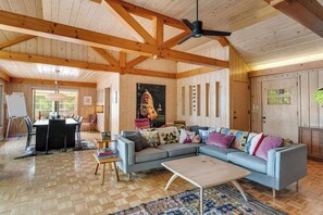 A spacious living room with a large sofa, a coffee table, and a dining area with a table and chairs. - Dog-friendly lakefront home with lake views, sauna, dock, firepit - near skiing (Land O'Lakes)