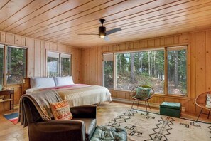 A wooden cabin bedroom with a bed, a chair, a rug, and large windows. - Dog-friendly lakefront home with lake views, sauna, dock, firepit - near skiing (Land O'Lakes)