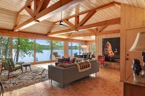 A spacious living room with large windows, a wooden ceiling, and a fireplace. - Dog-friendly lakefront home with lake views, sauna, dock, firepit - near skiing (Land O'Lakes)