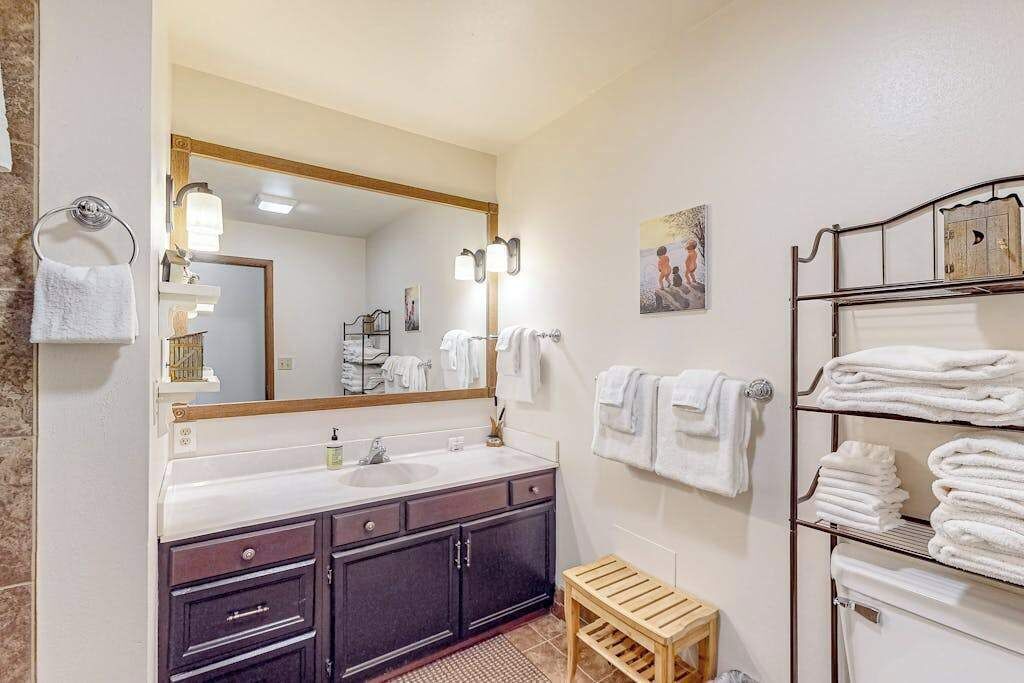 Une salle de bain avec un grand miroir, deux lavabos, un tabouret en bois et un porte-serviettes avec des serviettes pliées.