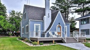 A two-story house with a wrap-around porch, a chimney, and a small deck with chairs.