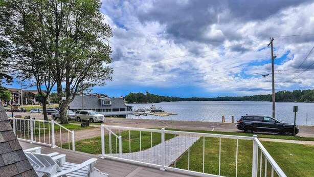 A deck with chairs overlooking a lake, a dock with boats, and a house with a grey roof.