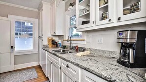 A kitchen with white cabinets, granite countertops, a coffee maker, and a window.