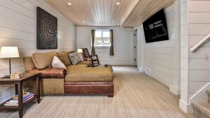 A cozy room with a brown leather sofa, a wooden ceiling, and a mounted TV.