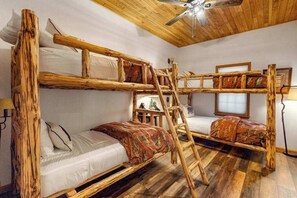 A bunk bed room with a wooden ladder, a ceiling fan, and a window with a view.