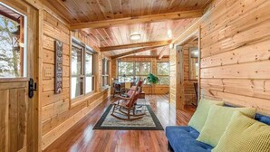 Ein Holzblockhaus-Interieur mit einer Couch, einem Schaukelstuhl und einem Essbereich.