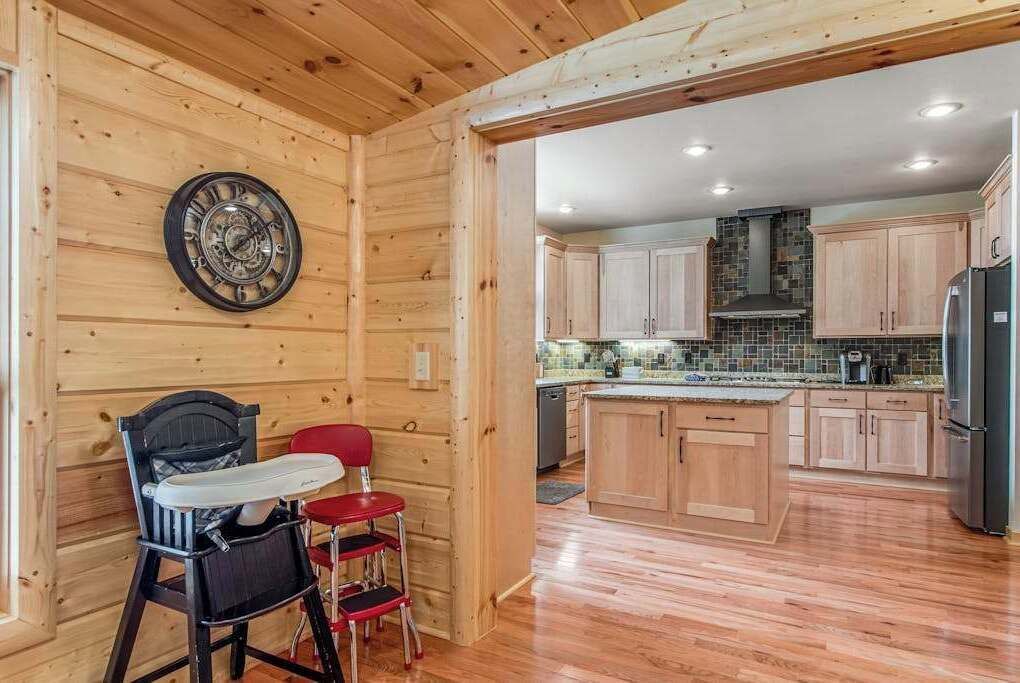 Un intérieur en bois avec un espace cuisine comprenant des meubles de rangement en bois, un dosseret carrelé et un réfrigérateur en acier inoxydable.