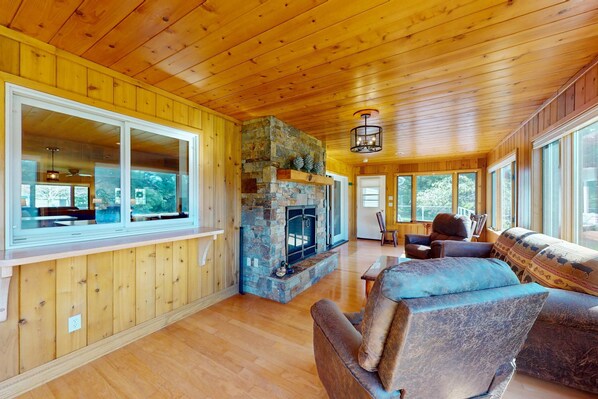 A wooden interior with a stone fireplace, large windows, and a cozy seating area.