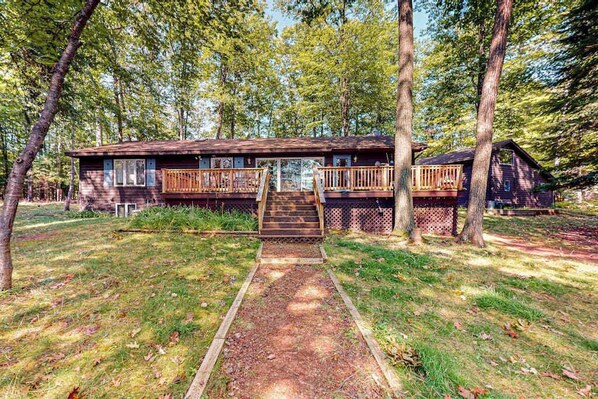 A cabin with a deck, a covered porch, and a pathway leading to the entrance.