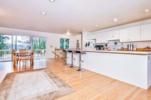A modern kitchen with white cabinets, a wooden countertop, and a bar area with stools.