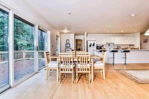 A modern kitchen with white cabinets, a dining area with wooden chairs, and a large sliding glass door leading to an outdoor deck.