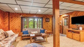 Un interior de cabaña acogedor con un sofá, una mesa de centro, un televisor y un mueble de madera.