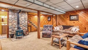 Una habitación acogedora con pared de piedra, estufa de leña azul, escalera de madera y un sofá con cojines estampados.