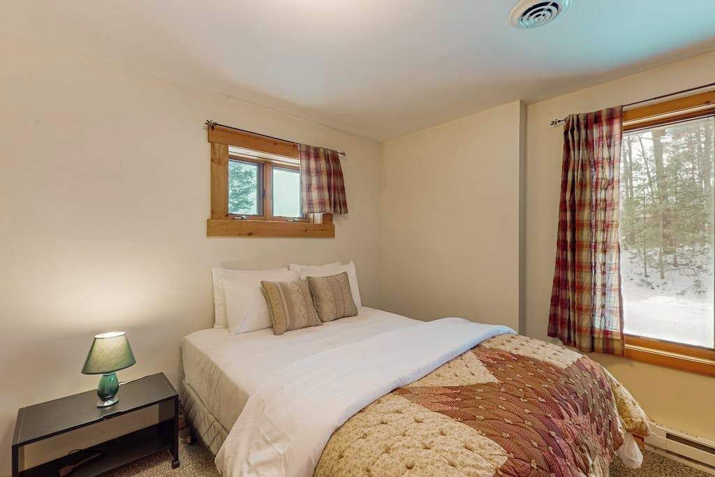 A bedroom with a bed, a nightstand, a window with curtains, and a view of trees outside.
