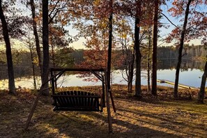 A wooden swing in a wooded area with a lake in the background.