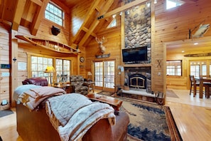 L’intérieur d’une cabane en rondins, avec une cheminée, un téléviseur et un lit recouvert de couvertures.