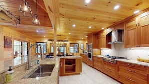 Una cocina amplia con gabinetes de madera, una isla central, electrodomésticos de acero inoxidable y encimera de granito.