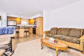 A living room with a sofa, a coffee table, and a chair. There is a kitchen in the background with wooden cabinets and a refrigerator. - Conveniently-located, dog-friendly home with a patio, central AC, & washer/dryer (Eagle River)