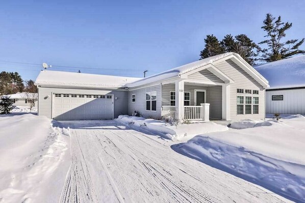 A white single-story house with a garage, a front porch, and a snow-covered driveway.