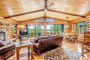 A spacious log cabin interior with a fireplace, leather sofa, dining area, and large windows. - Lakefront log cabin on 3.5 acres with dock, gazebo & sunset views - dog-friendly (Lac Du Flambeau)