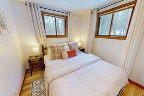 Un dormitorio con una cama grande, dos mesitas de noche, una mesilla auxiliar, una ventana y una puerta.