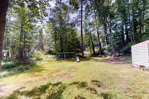 A backyard with a swing set, a shed, and a grassy area surrounded by trees.