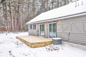 Eine Holzhütte mit einer Holzterrasse, großen Fenstern und einem mit Schnee bedeckten Dach.