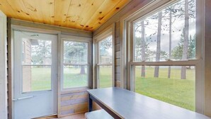 Ein Zimmer mit Holzboden, großen Fenstern, einer Bank und einer Tür, die nach draußen führt.