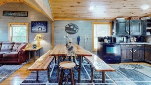 Ein rustikales Ferienhaus-Interieur mit einem Holzesstisch, einer Couch, einer Küchenzeile und einer an der Wand befestigten Uhr.