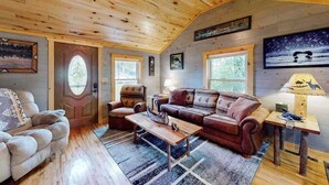 Ein gemütliches Blockhaus-Interieur mit Holzbalkendecke, einer Couch, einem Couchtisch und einer Lampe.