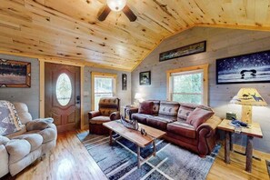 A cozy cabin interior with a wooden ceiling, a sofa, a coffee table, and a lamp. - Cozy home located near Lakes & Trails equipped with WIFI & a Gas Grill (Mercer)