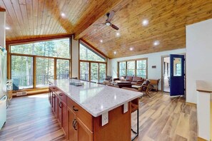 A spacious kitchen with a large island, wooden flooring, and large windows offering a view of the forest. - New Build-Serene Wooded Home with WIFI, Gas Grill, Near Lakes & Trails (Land O' Lakes)