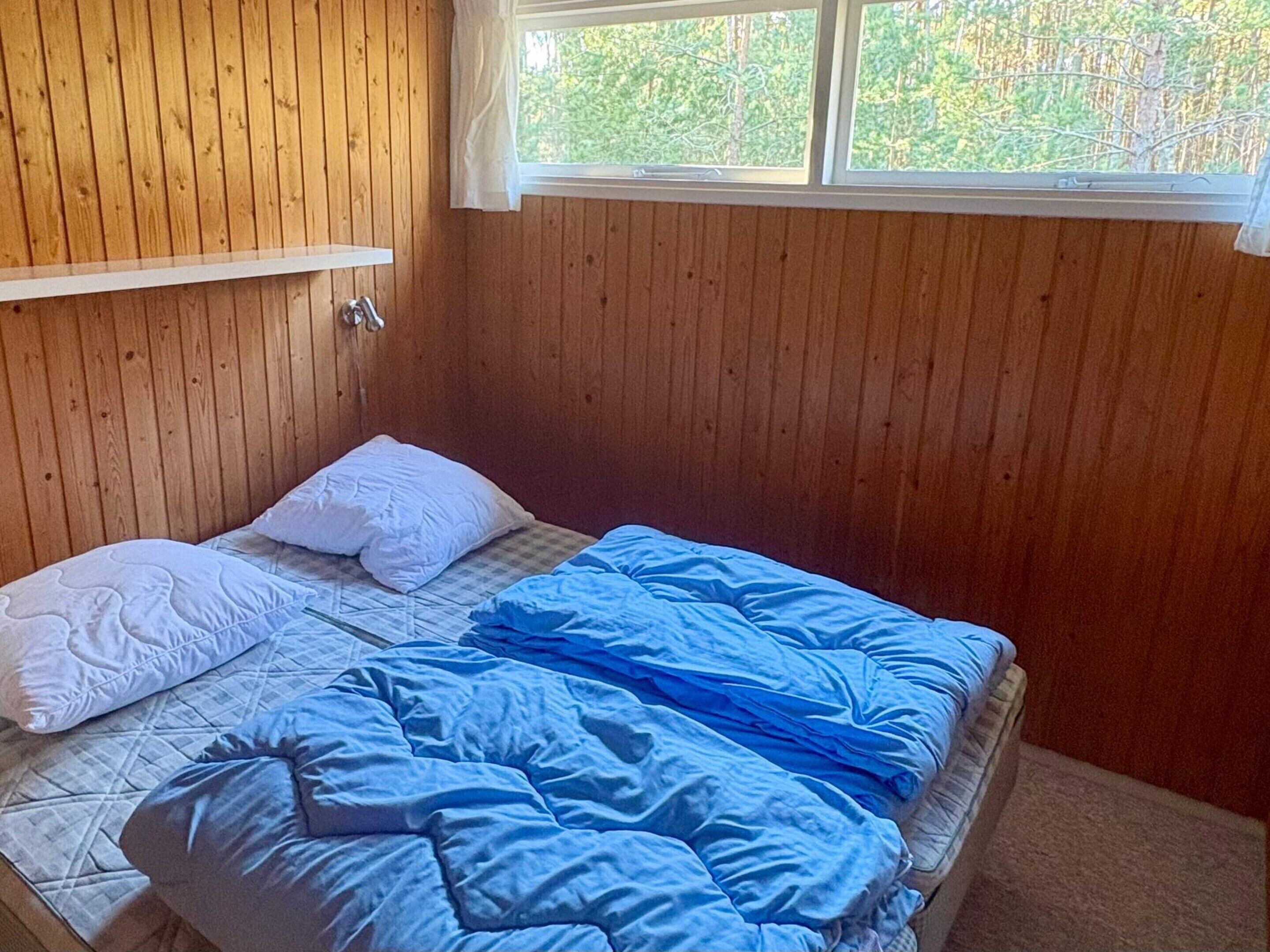 A single bed with white and blue bedding, a wooden headboard, and a window with a view of trees.